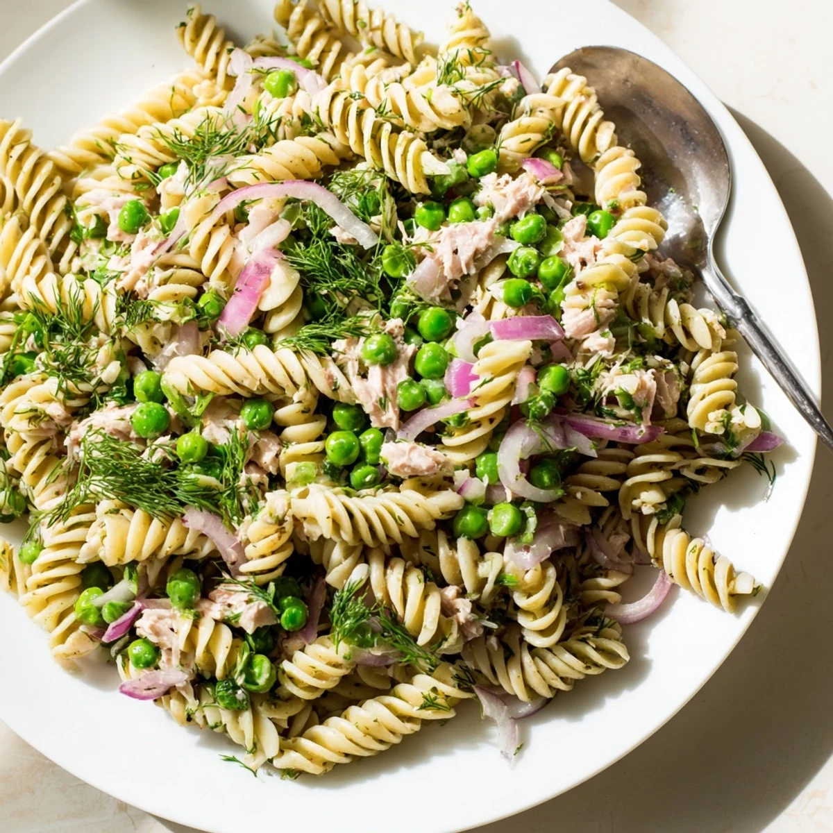 A vibrant serving of Lemony Tuna Pasta Salad with flaked tuna, green peas, and fresh parsley on a plate.  