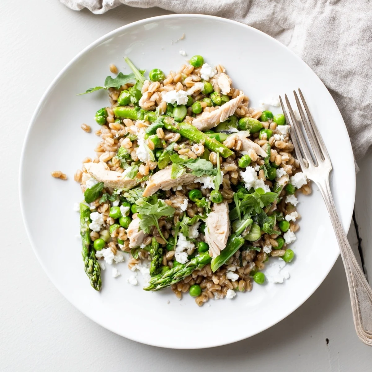 A vibrant bowl of Warm Spring Farro Chicken Salad featuring sliced seared chicken, blanched vegetables, and a zesty lemon dressing.