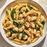 A close-up of One-Pot Spinach and Chicken Pasta, creamy with Parmesan cheese and herbs.