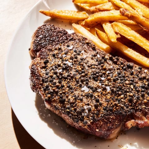Classic Peppercorn Ribeye: Sizzling, perfectly seared ribeye, glistening with peppercorns, alongside golden fries.