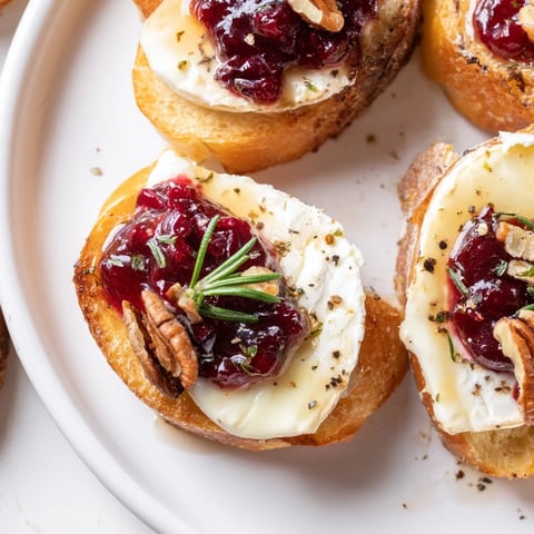 Warm, melty Brie tops toasted baguette rounds, piled high with cranberry sauce for Quick Cranberry Brie Crostini.