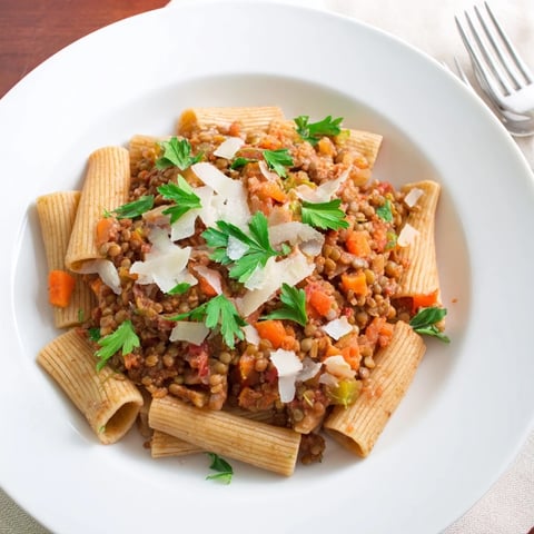 A steaming bowl of High-Fiber Lentil Bolognese over pasta, garnished with fresh parsley and Parmesan.