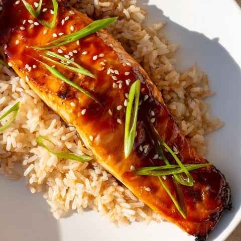 Sticky Orange Salmon, glistening with a vibrant glaze, sits atop fluffy rice, ready to eat.
