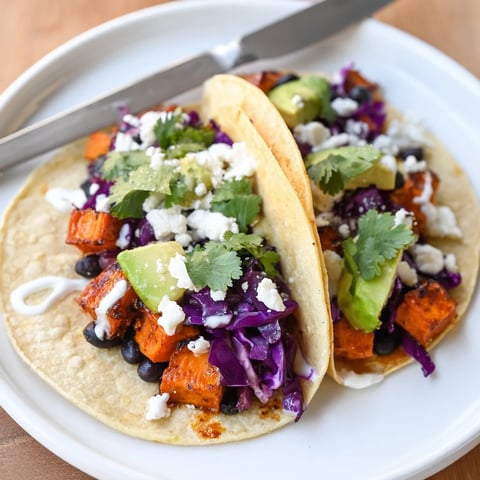 Golden roasted sweet potato and black bean tacos in warm corn tortillas, topped with avocado, red cabbage, and cilantro.