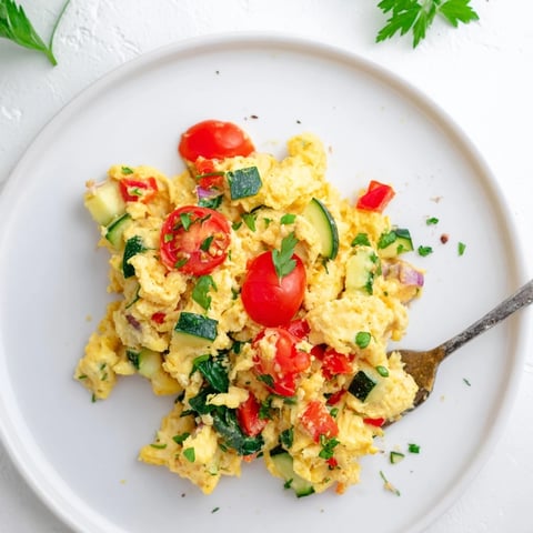 A fluffy Egg and Vegetable Scramble with cherry tomatoes, spinach, and bell peppers, served warm on a white plate.  