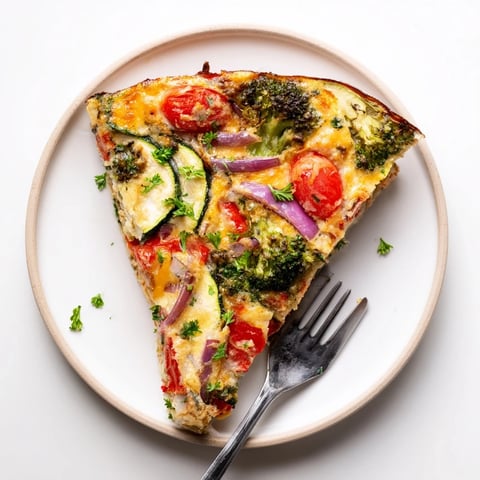 Golden-brown Vegetable Frittata baked in an oven-safe skillet, filled with broccoli, bell pepper, and cherry tomatoes.  
