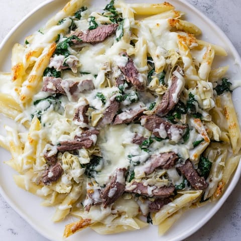 A close-up shot of the savory Steak & Spinach Artichoke Pasta Bake, bubbling with creamy sauce and golden cheese.