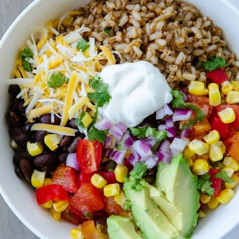 A vegetarian brown rice burrito bowl, featuring creamy queso and a bright, zesty lime wedge.
