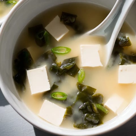 A close-up of steaming miso soup garnished with fresh scallions, perfect as a light Japanese appetizer or starter.  